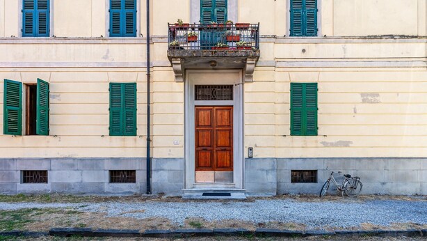 Un edificio con una porta centrale in legno, persiane verdi e una bicicletta parcheggiata fuori.