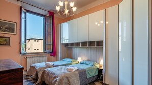 Una stanza con due letti, una finestra vista, un lampadario e un termosifone.