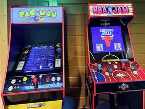 Deux bornes d’arcade, l’une portant l’inscription « PAC-MAN » et l’autre « NBA JAM », équipées de manettes et d’écrans de jeu.