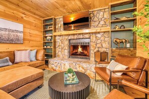 L’intérieur chaleureux d’un chalet avec une cheminée en pierre, des meubles en cuir et un téléviseur fixé au-dessus.