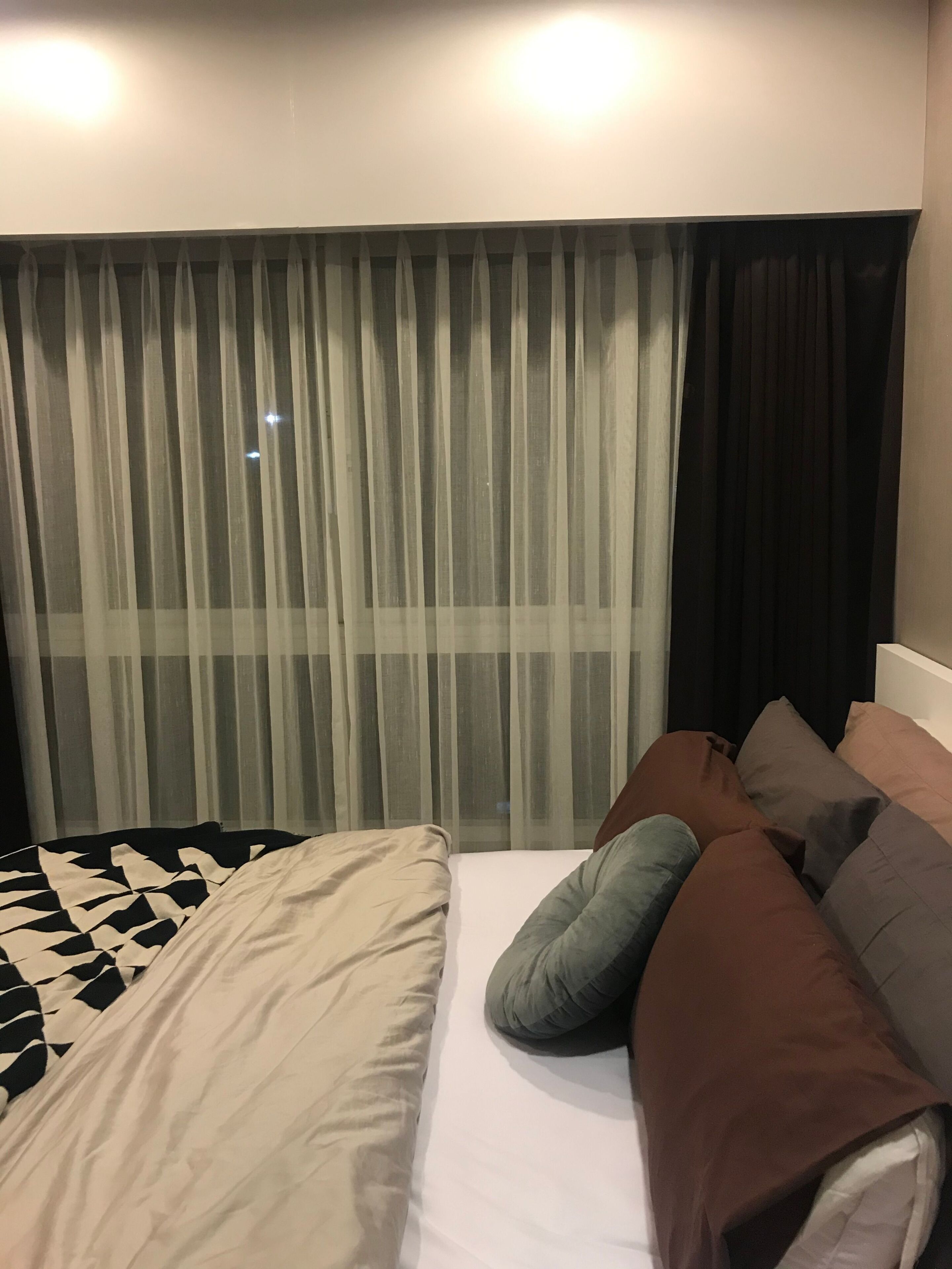 Una camera d'albergo con un letto, una finestra con tende leggere e una testiera.