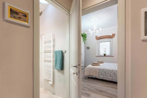 A room with a bed, a window with a plant, a chandelier, and a door leading to another room. - Civette A, Studio Apt with Shared Garden View (Greve in Chianti)