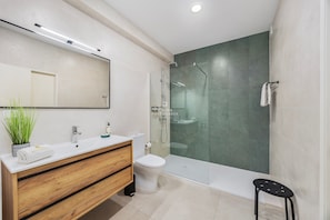 Un bagno moderno con doccia vetrata, un mobile bagno in legno, un water bianco e un piccolo sgabello.