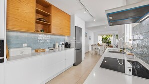 Uma cozinha moderna com armários brancos, geladeira de aço inoxidável, forno embutido e backsplash com azulejos azuis.