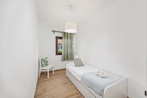Une petite chambre à coucher moderne, avec un lit simple, une chaise, une fenêtre donnant sur un beau paysage et un luminaire suspendu.