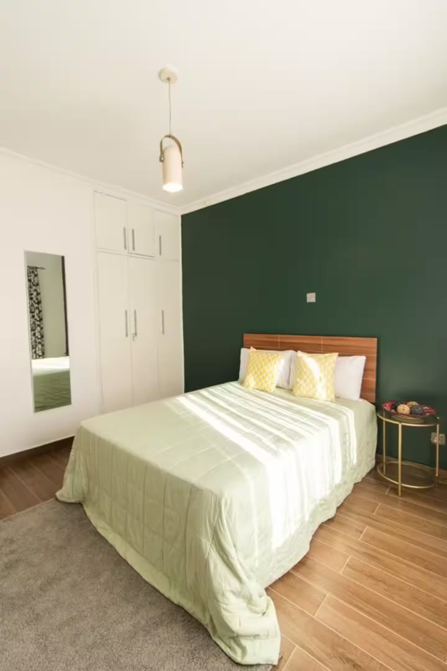 Een slaapkamer met een bed, een kledingkast, een spiegel en een klein rond tafeltje met een lamp.
