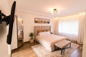 A bedroom with a large bed, a bedside table, a potted plant, a mirror, and a painting on the wall. - Gorgeous 3-bedroom apartment with AC in vibrant Nairobi (Nairobi)
