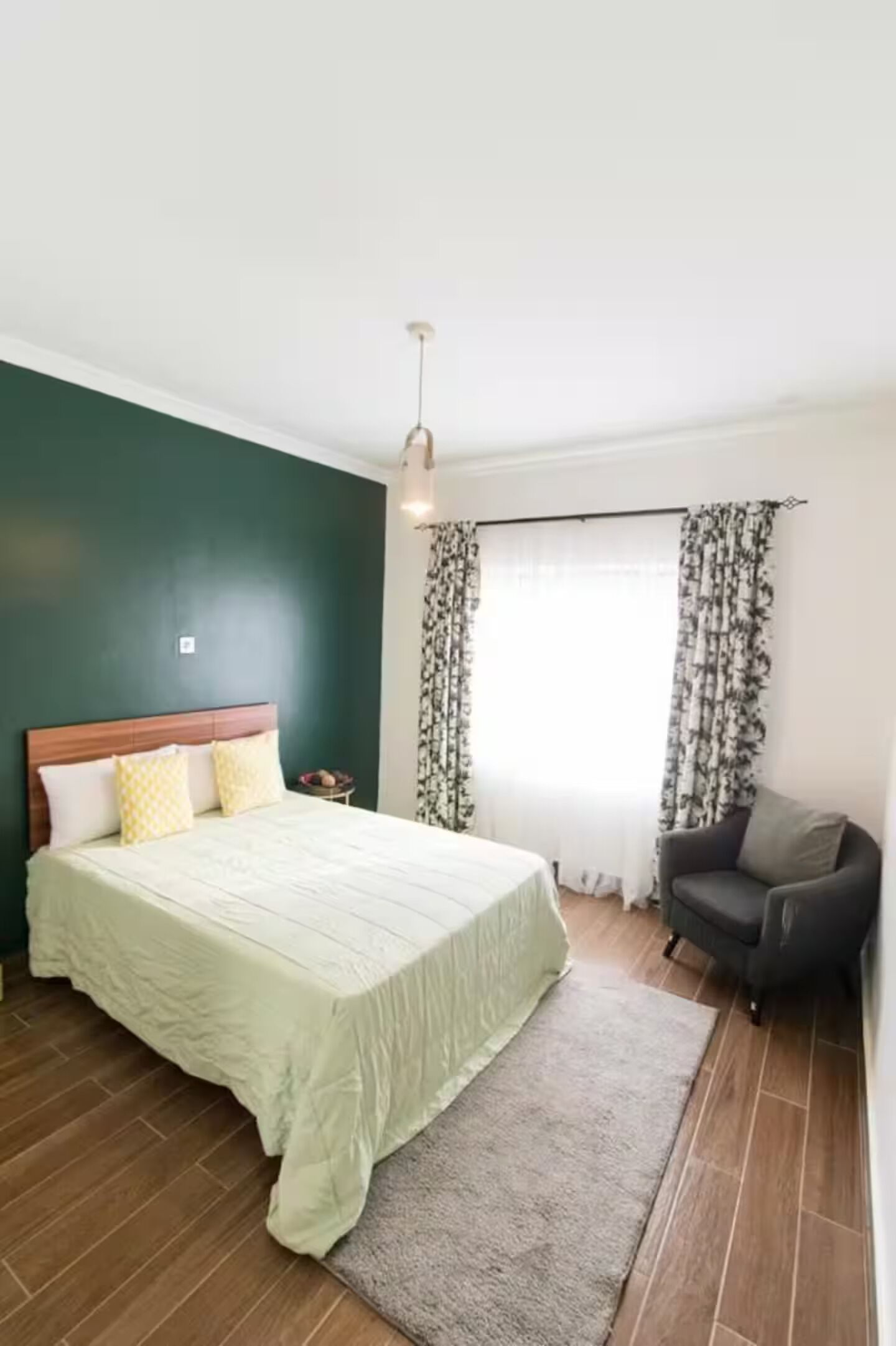 Une chambre à coucher avec un lit, une chaise, une fenêtre avec des rideaux et un plancher en bois.
