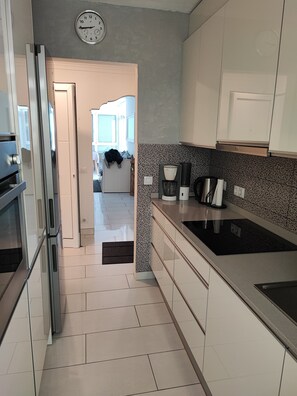Een moderne keuken met roestvrijstalen apparatuur, een betegelde spatwand en een zichtbare klok aan de muur.
