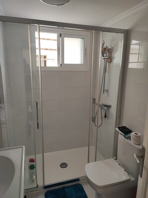 Une salle de bain avec une douche, des toilettes et une petite fenêtre.