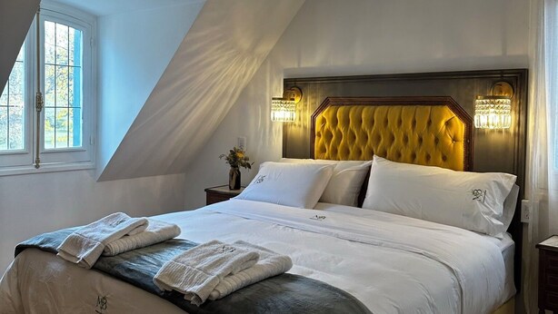 Ein Schlafzimmer mit einem großen Bett, einer Lüster, einem Fenster und einem Nachttisch mit einer Lampe.