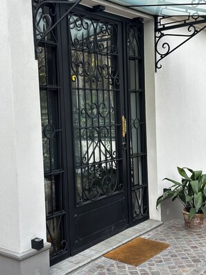 Ein schwarzes schmiedeeisernes Tor mit Glasscheibe, eine Fußmatte und ein Blumentopf.