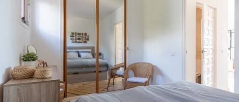 Un dormitorio con cama, armario, silla y una mesita con una planta.