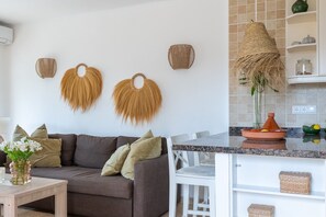 Ein modernes Wohnzimmer mit einem braunen Sofa, weißen Stühlen und einer Küchenzeile mit weißer Arbeitsplatte und Regalen.
