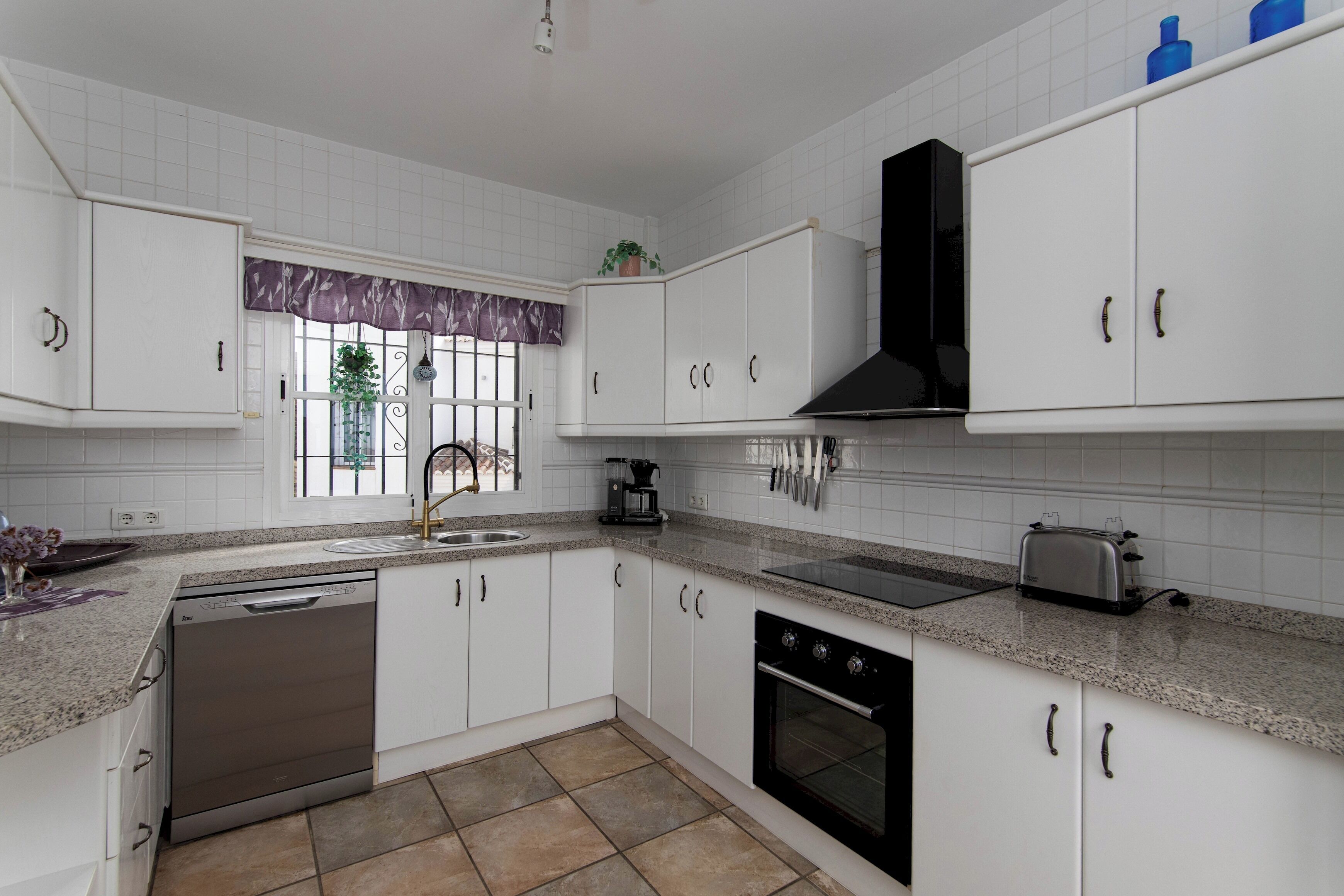 Une cuisine moderne avec des meubles blancs, un lave-vaisselle, un four et un grille-pain.