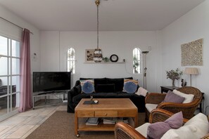 Ein Wohnzimmer mit Fernseher, Sofa, Couchtisch und Korbsesseln.