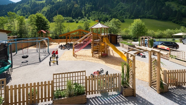 A playground with slides and swings, surrounded by a wooden fence and a mountain backdrop. - Apartment 'Gästehaus Egger 1' with Mountain View, Balcony and Wi-Fi (Grossarl)