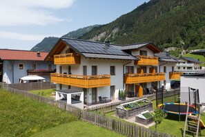 Ein zweistöckiges Gebäude mit Balkonen, einem Garten und Blick auf die Berge.