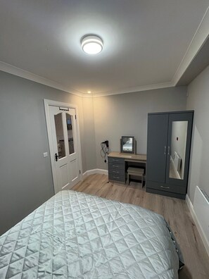 Un dormitorio con cama, escritorio, armario y puerta.