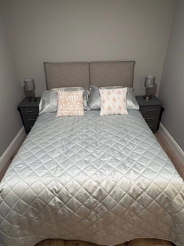 A bed with a quilted headboard, two bedside tables with lamps, and a plain wall.