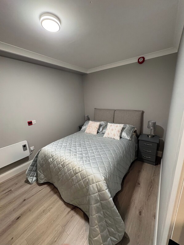 Un dormitorio con cama, mesitas de noche, enchufe en la pared y luz en el techo.