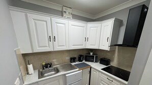 Una cocina compacta con armarios blancos, microondas integrado, cafetera y refrigerador pequeño.
