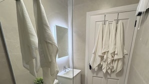 Un baño moderno con mampara de vidrio, inodoro, lavamanos y puerta con toallas colgadas.