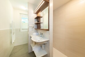 Ein modernes Badezimmer mit Waschbecken, Spiegel, Handtuchhalter und einem Fenster mit Jalousien.