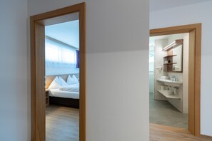 Ein Hotelzimmer mit Bett, Badezimmer mit Waschbecken und Spiegel sowie einem Holztürrahmen.
