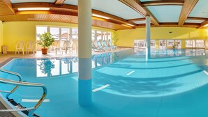 Une piscine intérieure avec des poutres en bois, des parois en verre transparent et des chaises longues.