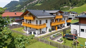 Une maison moderne à deux étages, dotée de panneaux solaires, d’une cour clôturée et d’un espace de jeux pour enfants.