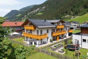 Una casa moderna de dos pisos con paneles solares, patio cercado y un parque infantil.