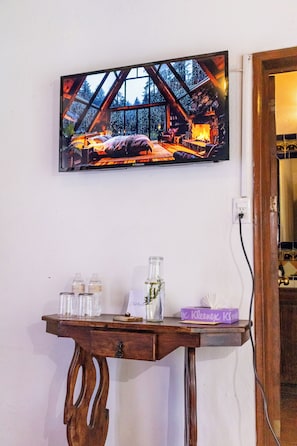 A wall-mounted television displaying a cozy cabin scene, a wooden table with a vase and a book, and a power outlet. - CasaLoreto Hotel Boutique (San Miguel de Allende)