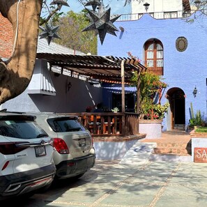 Un edificio con fachada azul, un patio cubierto y coches aparcados.