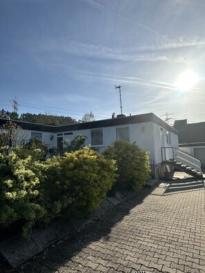 Un edificio residencial con una escalera que lleva al segundo piso, rodeado de vegetación y un cielo despejado.