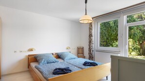 Een slaapkamer met een houten bed, een hanglamp, een nachtkastje en een raam met uitzicht op groen.