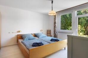A bedroom with a wooden bed, a hanging light fixture, a bedside table, and a window with a view of greenery. - Holiday Home 'Leni' with Shared Terrace and Garden (Edertal)