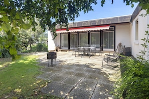 Eine Terrasse mit Tisch und Stühlen, einem Grill und einem überdachten Bereich mit Fenstern.