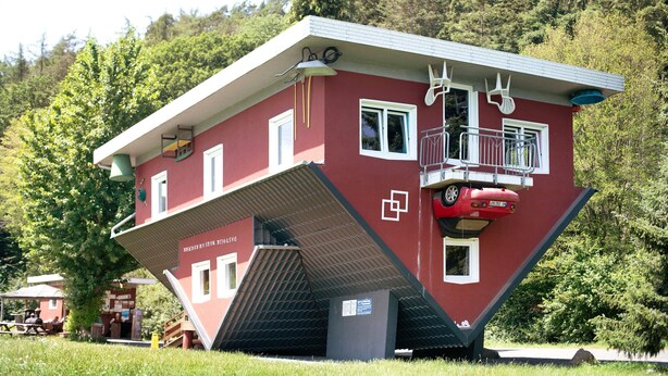 Een rood gebouw met een kenmerkend schuin dak, een balkon en een trap die naar een hoger gelegen niveau leidt.