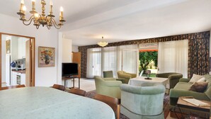 Een eetgedeelte met een tafel en stoelen, een televisie, en een woonkamer met banken en een kroonluchter.