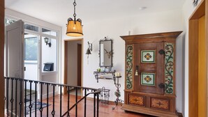 Een gang met een houten kast, een hanglamp en een deur naar een andere kamer.