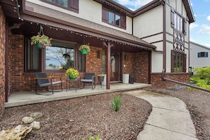 A two-story house with a porch, outdoor seating, hanging flower baskets, and a brick exterior.
