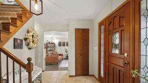 Un escalier en bois, une porte en bois avec des panneaux de verre, un salon avec un canapé et un couloir avec un paillasson.
