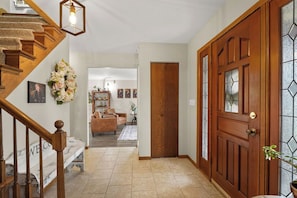 A wooden staircase, a wooden door with glass panels, a living room with a sofa, and a hallway with a welcome mat.