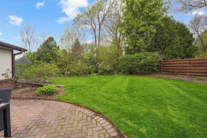 A well-maintained backyard with a paved patio area, a lawn, and a wooden fence.