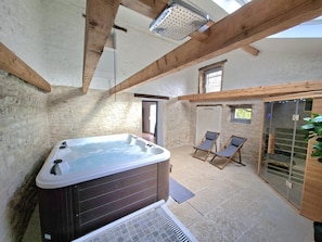 Un espace spa comprenant un jacuzzi, deux chaises longues et une porte vitrĂ©e donnant sur lâextĂ©rieur.