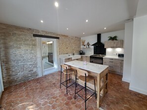 A kitchen with a stone wall, a tiled floor, a central island with stools, and modern appliances.
