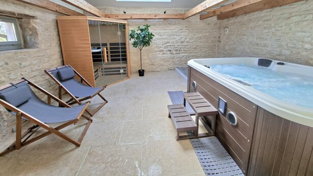 Ein Wellnessbereich mit Whirlpool, Holzliegen, einer Glastür zu einer Sauna und einem Oberlicht.
