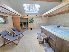 A spa area with a hot tub, wooden lounge chairs, a glass door leading to a sauna, and a skylight.