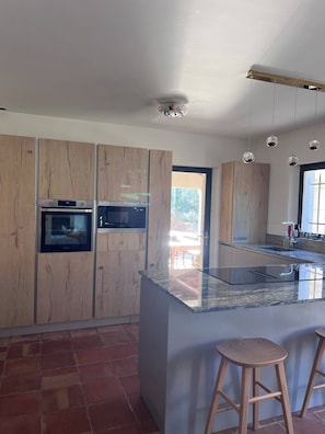 Eine moderne Küche mit Holzschränken, Edelstahlgeräten, einer Granitarbeitsplatte und Pendelleuchten.